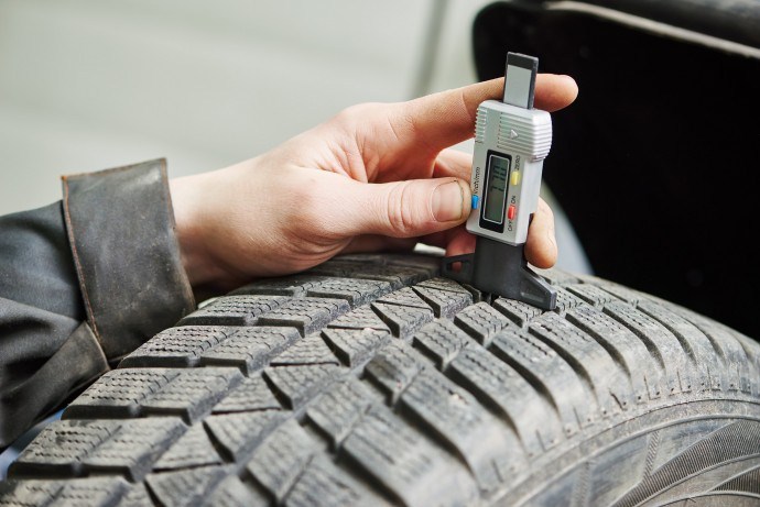 auto service man worker measuring rubber car wheel tyre protector